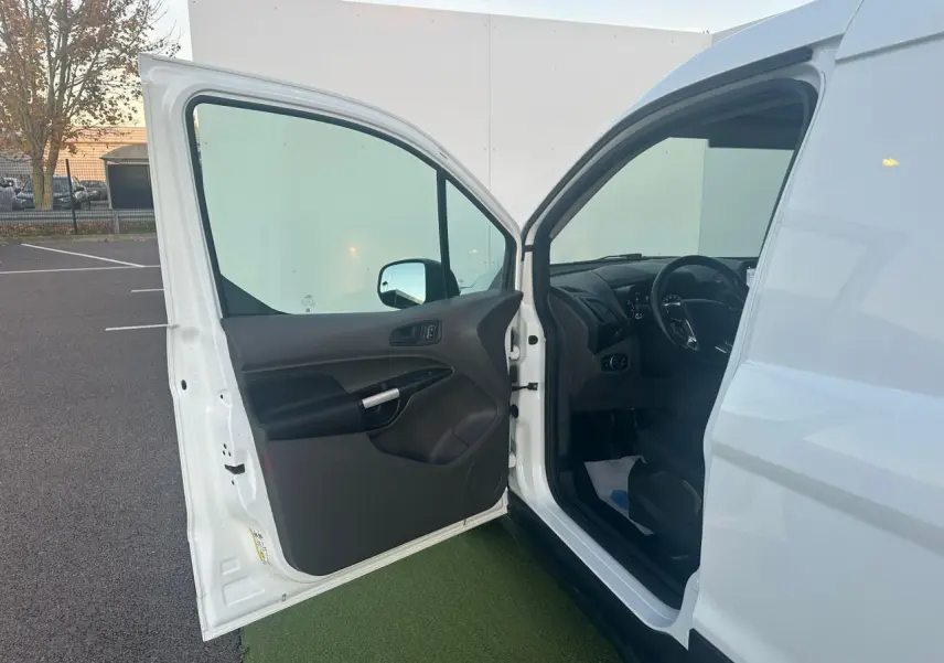 Portière avant gauche ouverte d'un Ford Transit Connect blanc, montrant l'intérieur noir et le tableau de bord côté conducteur.