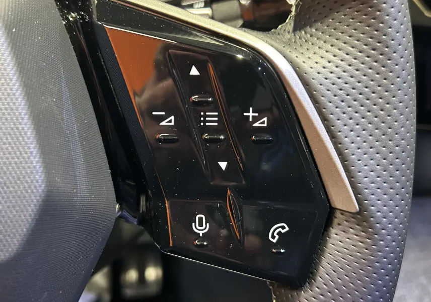 Gros plan sur les commandes multifonctions à gauche du volant perforé du Peugeot 3008 gris Artense 2025.