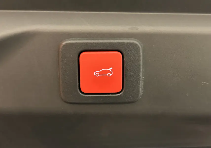 Bouton rouge d'ouverture électrique du hayon sur Peugeot 3008 gris Artense, vue rapprochée intérieure du coffre.