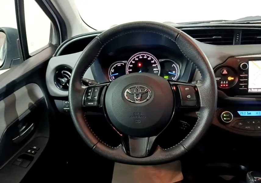 Vue intérieure centrée sur le volant cuir et alu de la Toyota Yaris blanche, avec tableau de bord et écran tactile visibles.