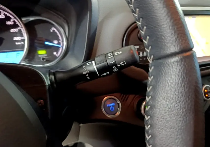 Gros plan sur le volant cuir et le bouton démarrage bleu de la Toyota Yaris 1.5 Hybride, tableau de bord partiellement visible.