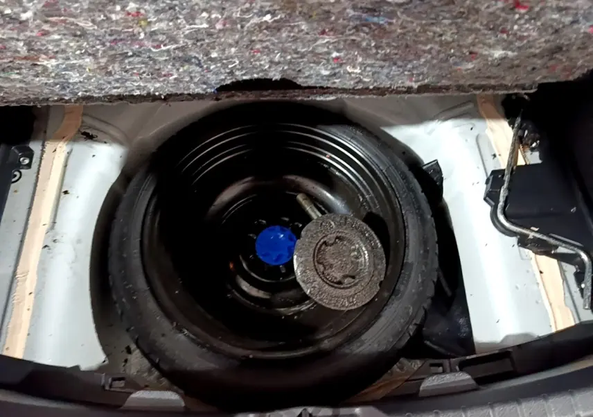 Vue plongeante sur la roue de secours noire dans le coffre d'une Toyota Yaris blanche, avec tapis de coffre partiellement visible.