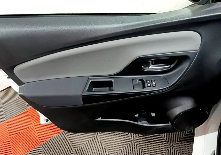 Vue rapprochée de la porte avant gauche de la Toyota Yaris blanche, montrant les commandes des vitres et la poignée intérieure.