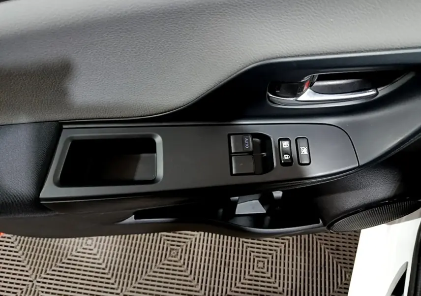 Gros plan sur la commande de lève-vitres et la poignée intérieure côté conducteur d'une Toyota Yaris blanche.