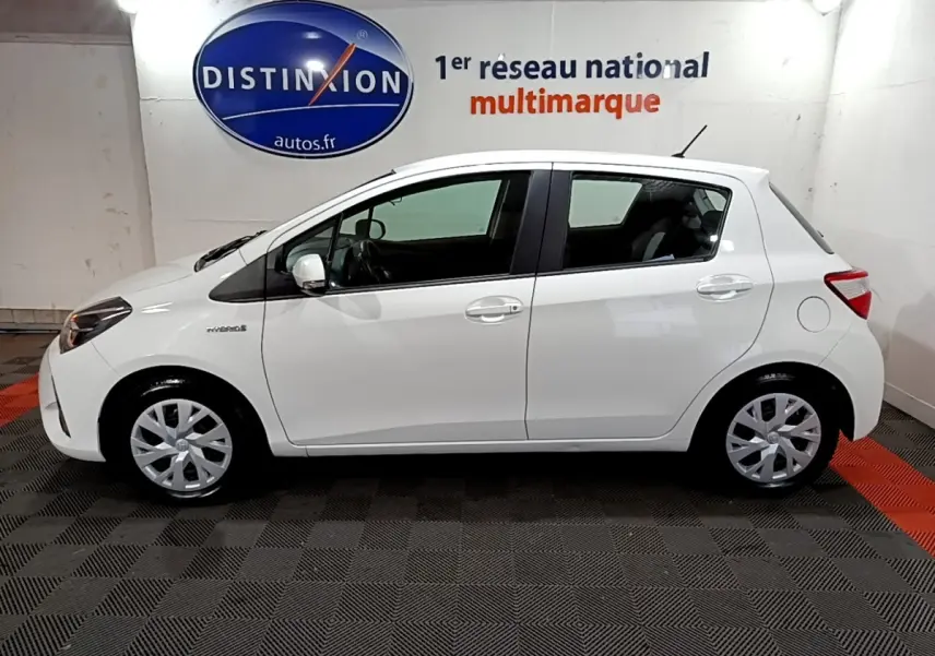 Profil côté gauche d'une Toyota Yaris 1.5 Hybride blanche, avec jantes alliage et logo hybride visible sur l'aile avant.