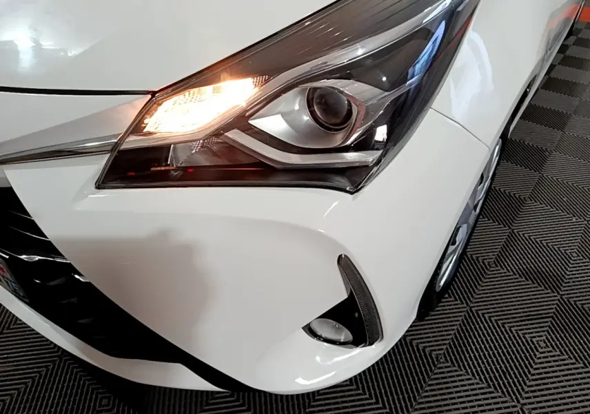 Gros plan sur l'avant droit blanc de la Toyota Yaris 1.5 Hybride, phare allumé et antibrouillard visible.