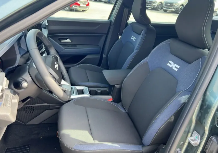 Vue intérieure côté conducteur du Dacia Bigster Hybrid 155 Expression Plus avec sièges bi-matière noirs et bleus et accoudoir central.