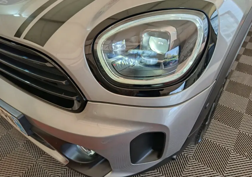Gros plan sur le phare avant droit et la calandre d’une MINI Countryman gris foncé 2023, finition Cooper Edition Premium Plus.