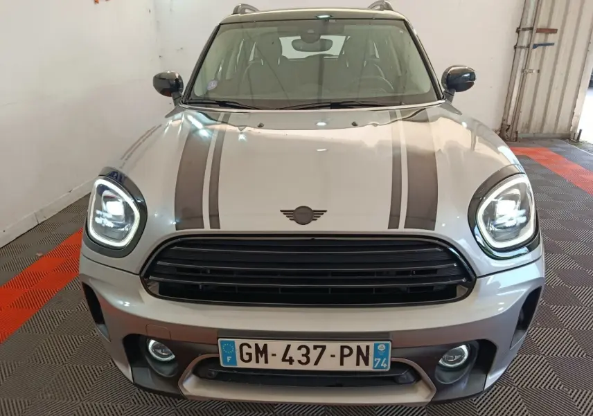 Vue avant d'une MINI Countryman gris foncé avec bandes noires sur le capot et phares LED allumés.