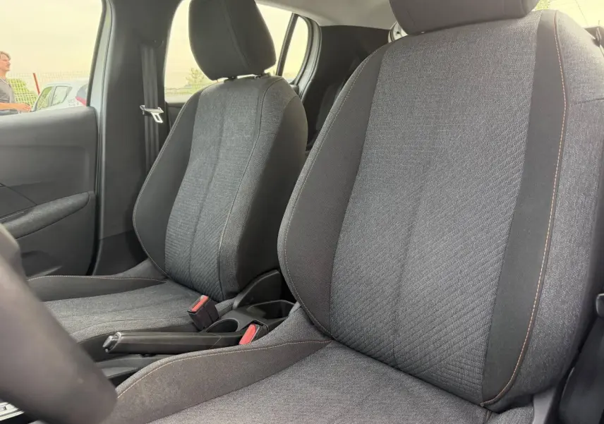 Vue intérieure rapprochée des sièges avant en tissu gris avec surpiqûres orange dans une Peugeot 208 blanche.