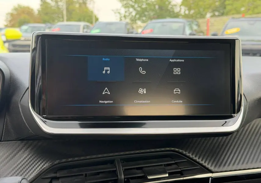 Écran tactile central affichant les menus radio, téléphone, navigation et climatisation dans l'habitacle du Peugeot 208 blanc.