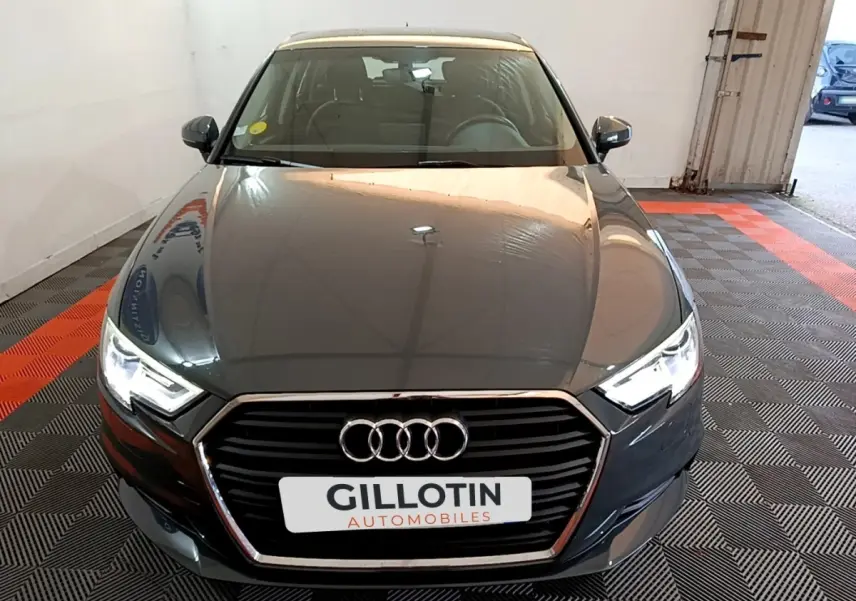 Vue avant d'une Audi A3 30 TDI gris foncé avec phares LED allumés dans un garage.