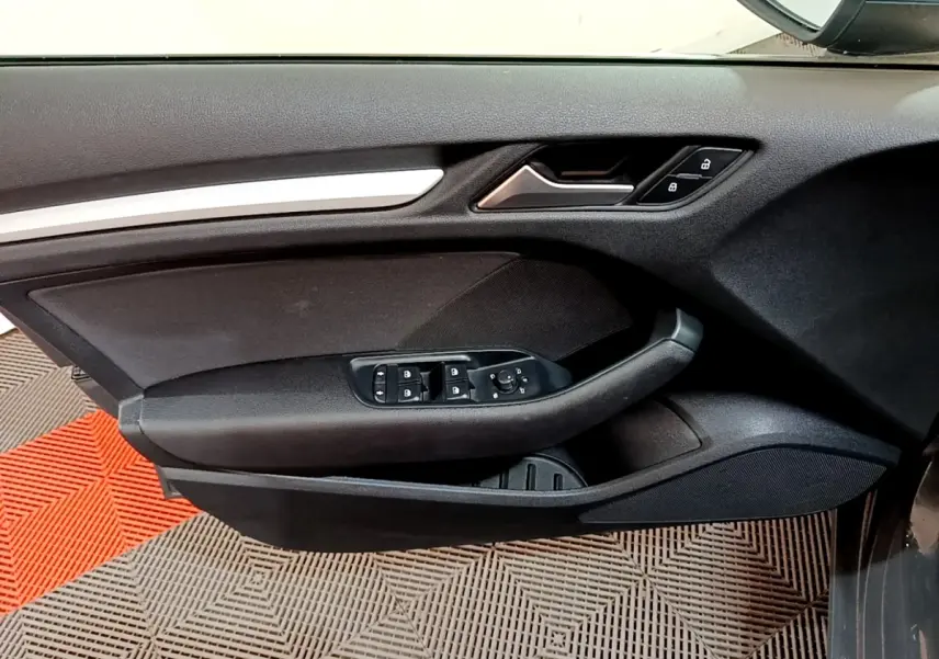 Vue rapprochée de la porte avant gauche d’une Audi A3 gris foncé, avec commandes électriques et verrouillage central.