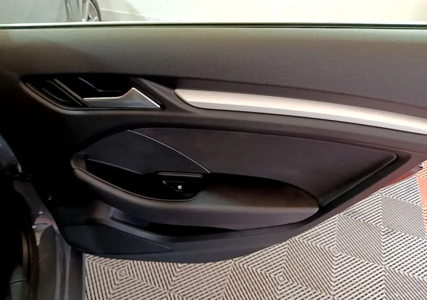 Vue intérieure côté gauche de la porte avant d'une Audi A3 gris foncé avec garniture noire et poignée argentée.