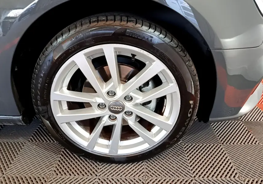 Gros plan sur la roue avant droite d'une Audi A3 gris foncé, jante alliage à plusieurs branches, pneu Pirelli visible.