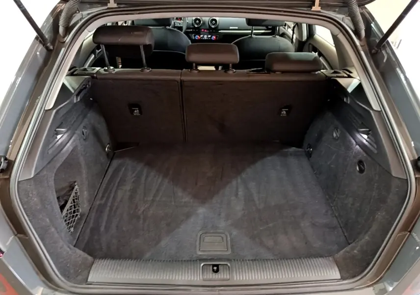 Coffre ouvert vu de l'arrière d'une Audi A3 gris foncé, montrant l'espace de chargement et la banquette arrière.