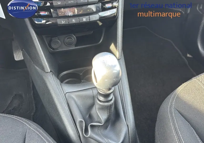 Le levier de vitesses manuel de la Peugeot 208 noir perle métal vu de dessus avec la console centrale et les sièges partiellement visibles.