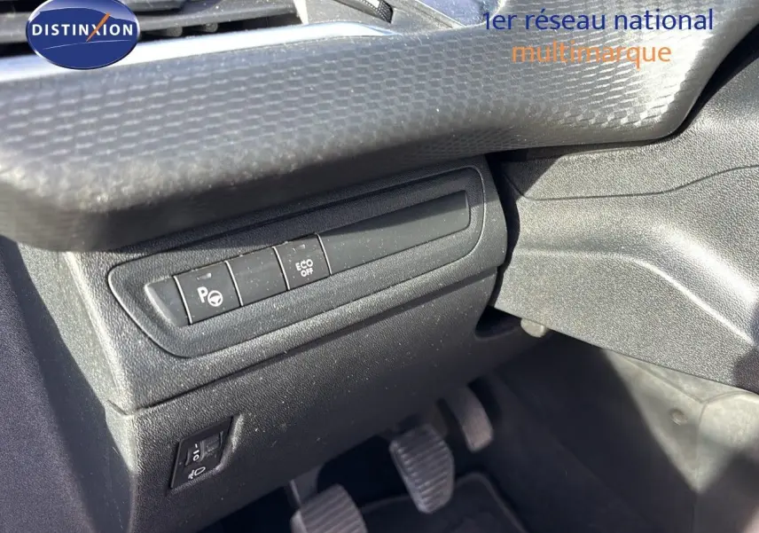 Détail des commandes côté conducteur du tableau de bord noir avec pédales d’embrayage, frein et accélérateur visibles.