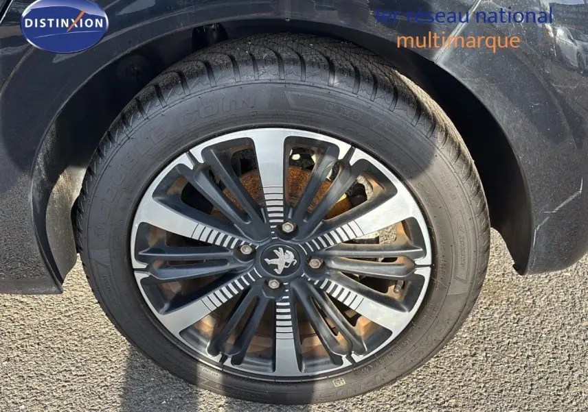 Gros plan sur la roue avant gauche d'une Peugeot 208 noire perle métal avec jante alliage distinctive.