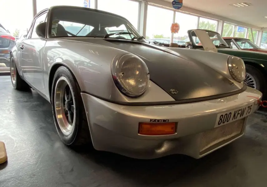 Porsche 911 3.0 SC gris métallisé vue 3/4 avant avec capot noir mat et jantes Fuchs noires.