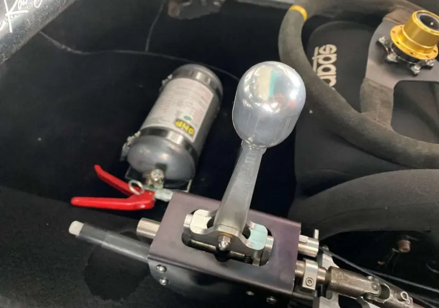 Gros plan sur le levier de vitesse manuel rigide et extincteur dans l'habitacle d'une Porsche 911 3.0 SC gris métallisé.