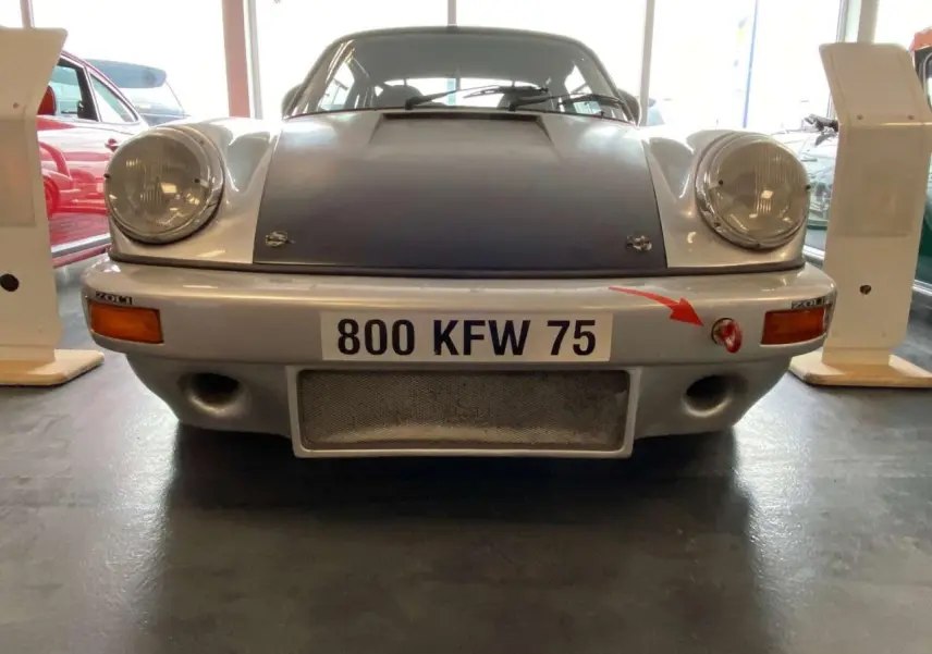 Vue frontale d'une Porsche 911 3.0 SC 930 gris métallisé avec capot noir mat et attache rouge sur pare-chocs.