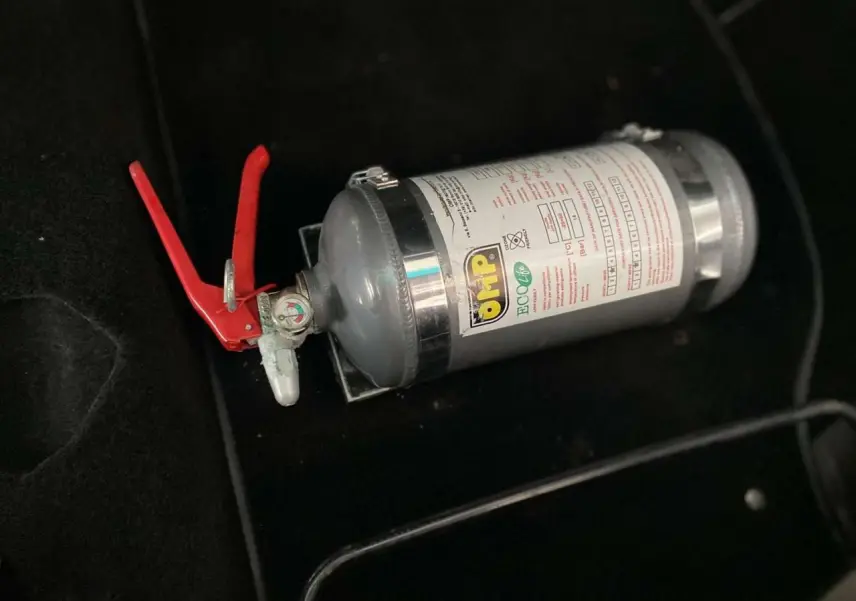 Extincteur gris avec poignée rouge posé sur le sol noir de l'habitacle d'une Porsche 911 3.0 SC 1980.