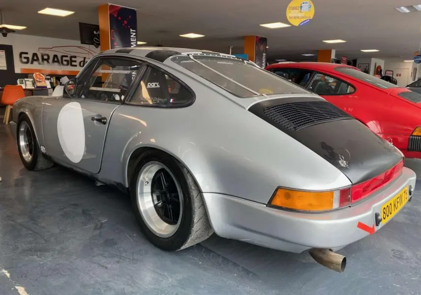 Vue 3/4 arrière droite d'une Porsche 911 3.0 SC gris métallisé avec jantes Fuchs et capot arrière noir mat.