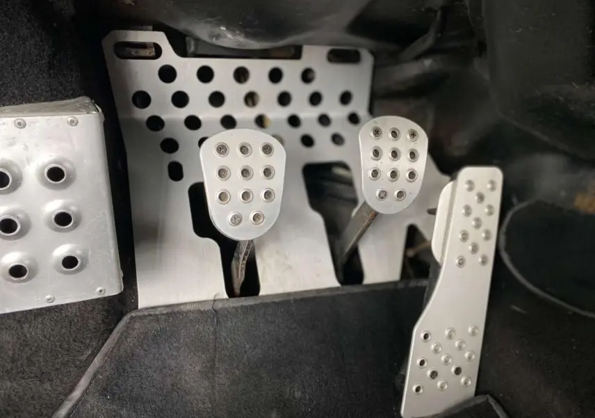 Gros plan sur les pédales en aluminium perforé d'une Porsche 911 3.0 SC 930 gris métallisé de 1980 avec boîte manuelle.