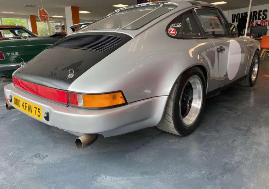 Vue 3/4 arrière droite d'une Porsche 911 3.0 SC gris métallisé avec jantes Fuchs et capot arrière noir mat.