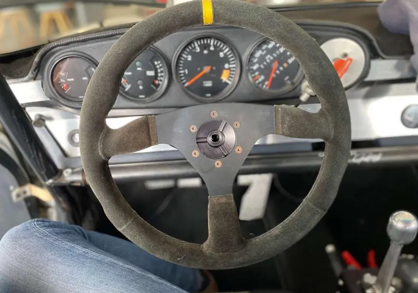 Volant Sparco en alcantara avec moyeu débrayable, tableau de bord et compteurs d'une Porsche 911 3.0 SC gris métallisé vue de l'intérieur.