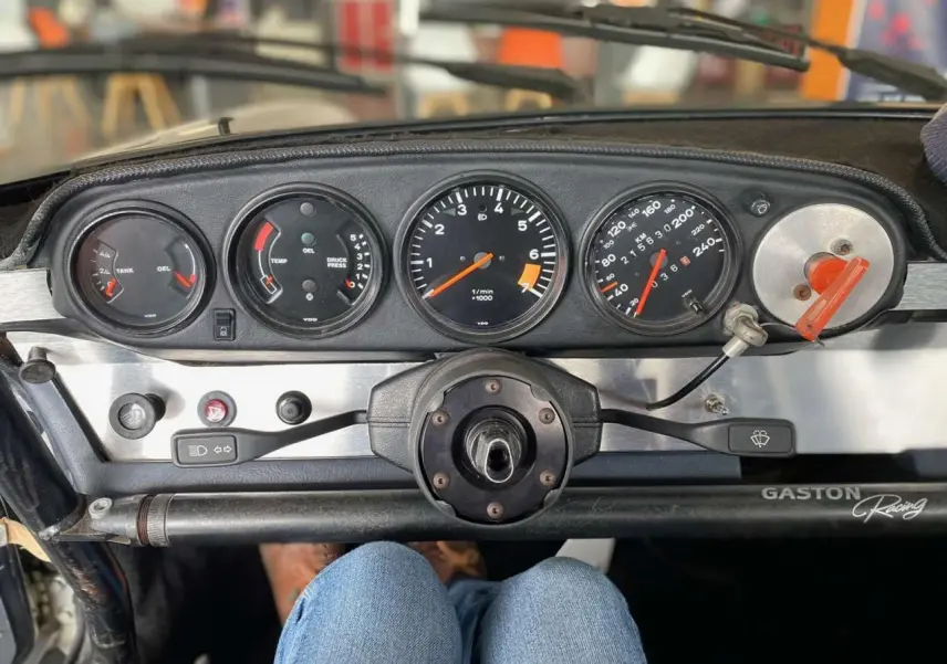 Tableau de bord en aluminium brossé d'une Porsche 911 3.0 SC 1980, avec compteurs ronds et arceau de sécurité visible.