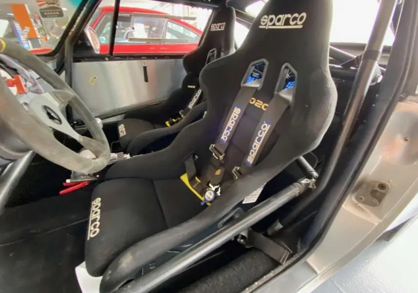 Intérieur de Porsche 911 3.0 SC gris, vue côté gauche sur baquets Sparco noirs avec harnais et arceau tubulaire.