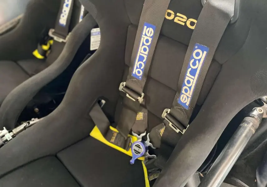 Gros plan sur les baquets noirs Sparco avec harnais 6 points dans une Porsche 911 3.0 SC gris métallisé de 1980.