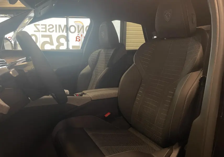 Vue intérieure côté conducteur du Peugeot 3008 2025, sièges tissu et cuir noir avec logo Peugeot brodé sur les appuie-têtes.