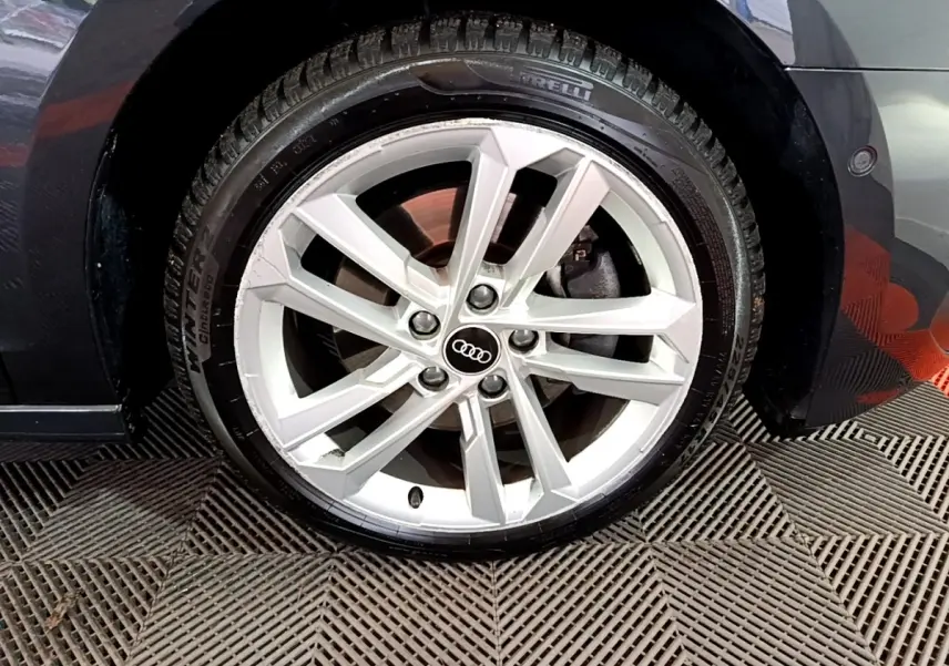 Gros plan sur la roue avant droite d'une Audi A3 gris foncé, avec jante alliage et logo Audi au centre.