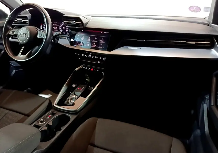 Vue intérieure côté conducteur de l'Audi A3 gris foncé, avec volant cuir multifonctions et écran tactile central.