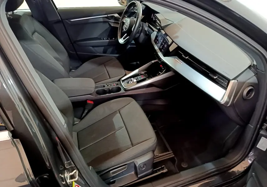 Vue intérieure côté conducteur de l'Audi A3 gris foncé, mettant en valeur le volant cuir multifonctions et le tableau de bord digital.