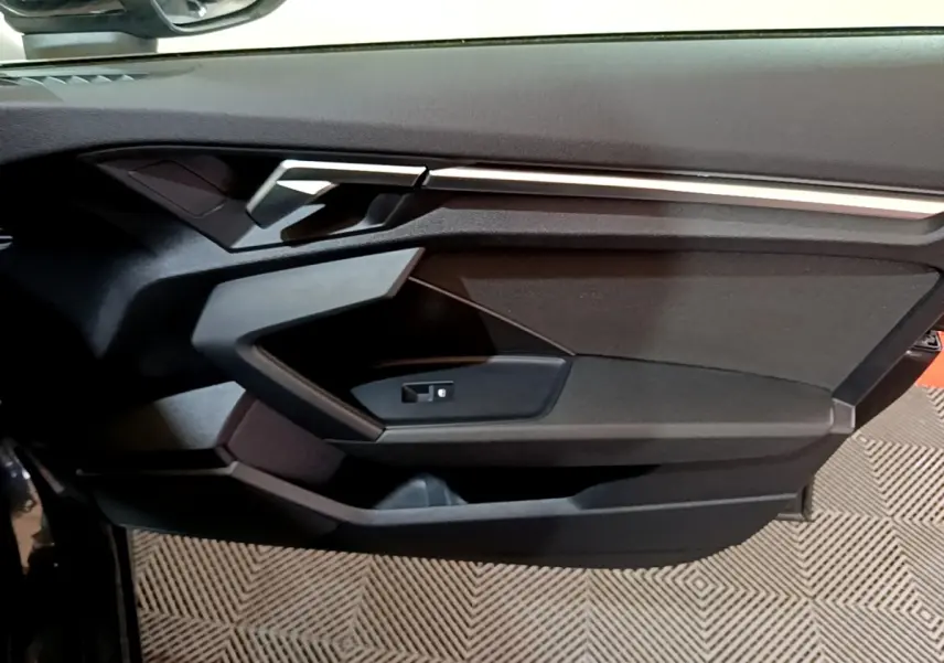 Vue rapprochée de la porte côté conducteur de l'Audi A3 gris foncé, mettant en valeur la poignée et les commandes de vitre.