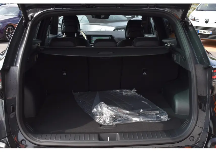Coffre ouvert vu de l'arrière d'un KIA SPORTAGE noir 2026, avec intérieur spacieux et tapis plastique au sol.