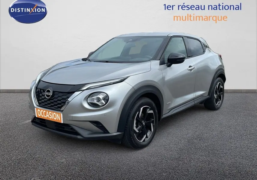 Nissan Juke Hybrid gris perle métal en 3/4 avant droit, avec jantes noires et calandre noire distinctive.