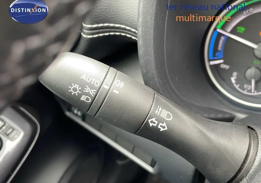 Gros plan sur la commande des feux et clignotants du tableau de bord d'un Nissan Juke gris perle hybride 2023.