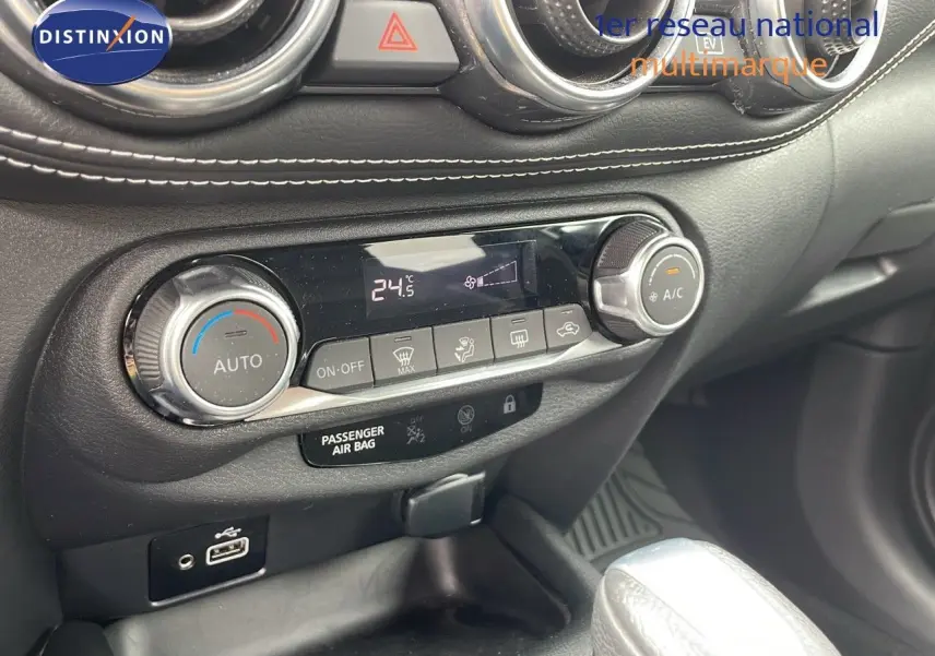 Gros plan sur la console centrale du Nissan Juke Hybrid 2023, avec commandes climatisation et finition cuir noire.