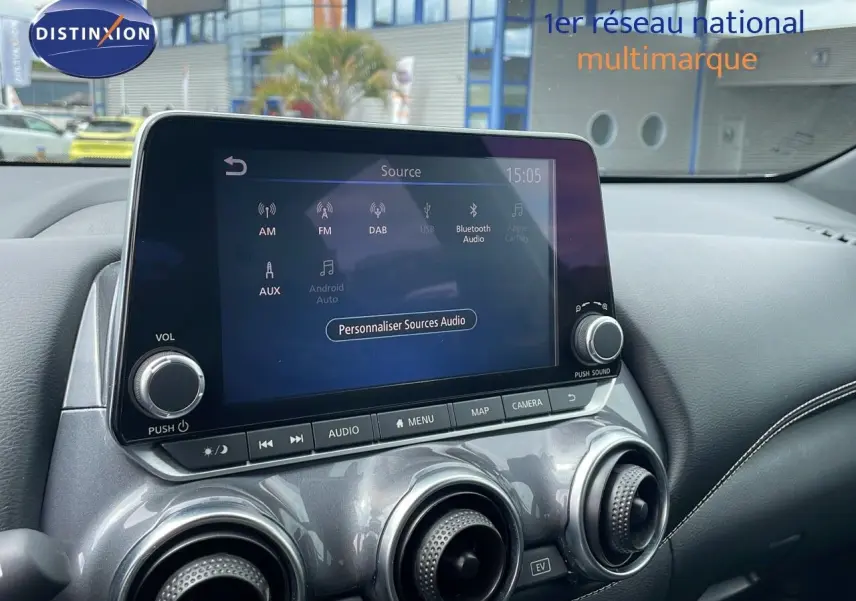 Vue intérieure centrée sur l'écran tactile et les aérateurs ronds du tableau de bord gris perle métallisé du Nissan Juke Hybrid 2023.