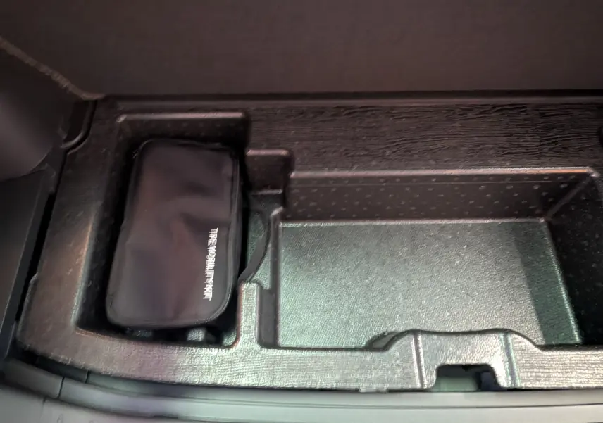 Rangement intérieur avec trousse de mobilité noire dans le compartiment central du Kia Sportage blanc MY25.