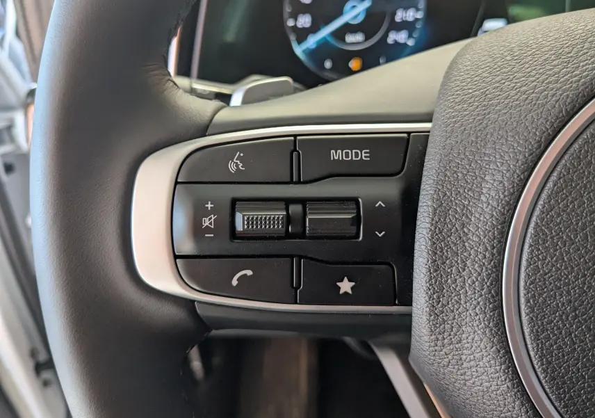 Gros plan sur les commandes au volant du Kia Sportage blanc MY25, mettant en valeur les boutons multifonctions côté gauche.