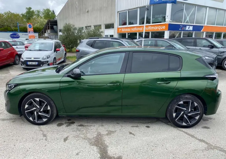 Profil latéral droit d'une Peugeot 308 2023 vert olivine avec jantes alliage 17 pouces et vitres surteintées.