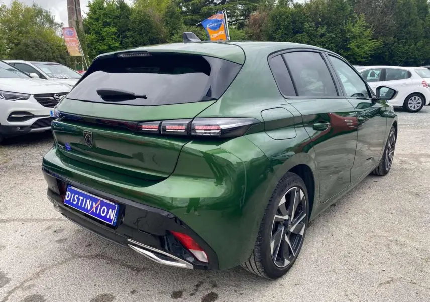 Vue 3/4 arrière droite d'une Peugeot 308 2023 vert olivine avec jantes alliage et vitres surteintées.