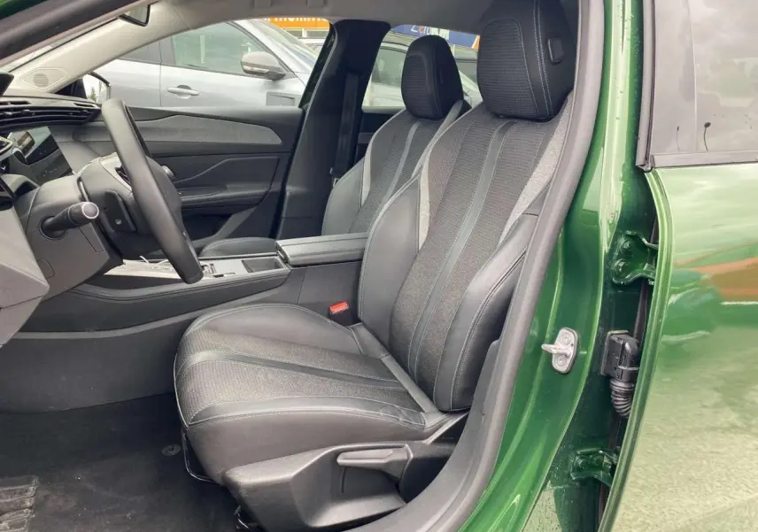 Vue côté gauche intérieur de la Peugeot 308 2023 vert olivine, sièges avant en cuir et tissu gris avec console centrale.