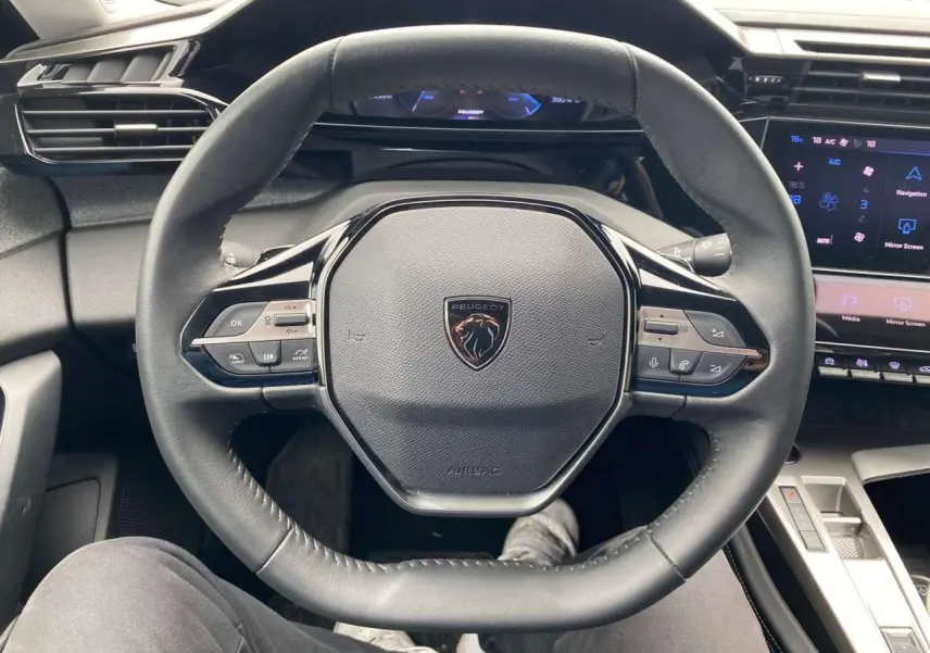 Volant cuir noir de Peugeot 308 2023 vu de face, avec commandes intégrées et tableau de bord numérique bleu.